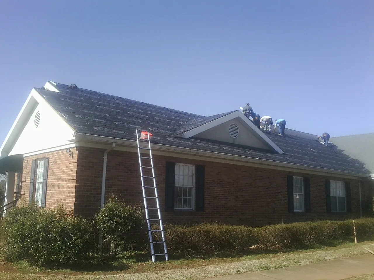 Crew tearing shingles off a brick ranch roof with a ladder set — Emergency Roof Repair work by our crew in Bullville