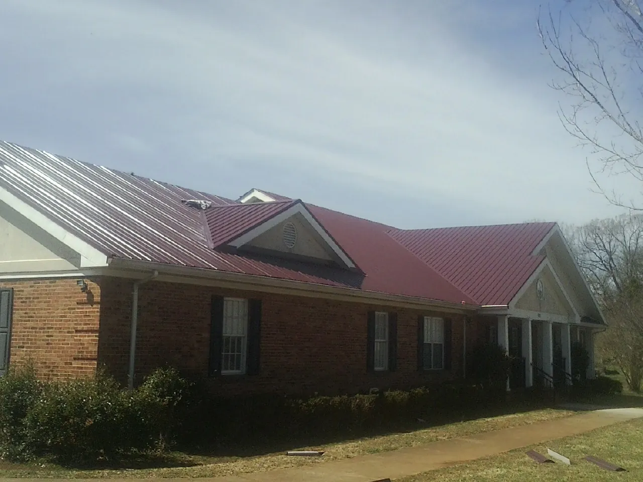 Red metal roof with gabled entries on a long brick building, from a Hail Damage Roof Repair job in Bullville