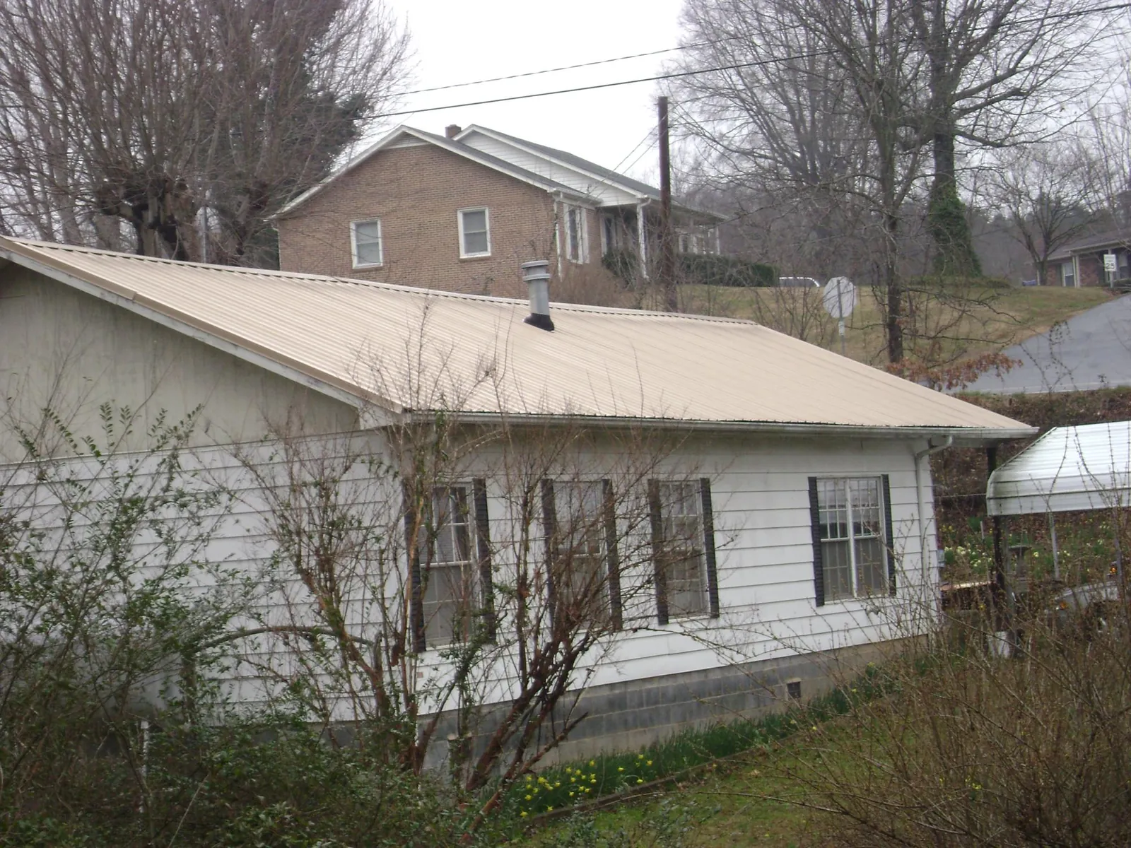 Tan metal roof on a white sided house set into a hillside — Commercial Roofing by Roofing Brothers in Bullville